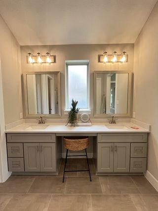 A chic bathroom featuring dual sinks, elegant lighting, and a stylish vanity with a woven stool.
