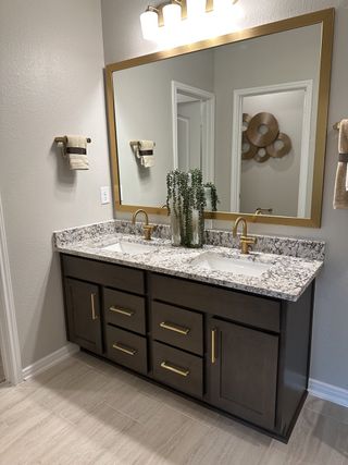 Model Home A modern bathroom with a sleek double vanity, granite countertop, gold fixtures, and elegant lighting.