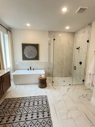 Model Home A spacious bathroom with a freestanding tub, glass shower, and elegant tiles, complemented by a decorative rug and soft lighting.