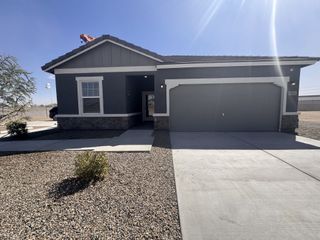 Street view A modern dark gray home with stone accents and a two-car garage in Agave Trails by Starlight Homes (Buckeye, AZ).