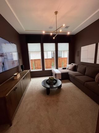 A cozy living room with dark walls, a modern light fixture, plush sectional, and large windows illuminating the space.