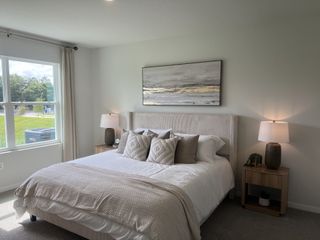 A serene bedroom with a neutral palette, featuring a plush bed, soft linens, and a large window overlooking a green landscape.