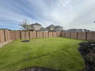 A spacious backyard with lush green grass and a wooden fence in Highland Village by Pulte Homes (Georgetown, TX).