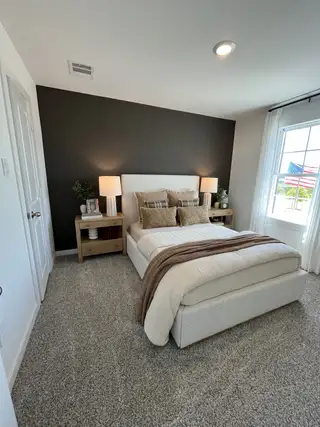 Model Home A cozy bedroom featuring a dark accent wall, plush carpeting, and soft lighting from bedside lamps.