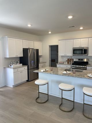 A modern kitchen with sleek appliances, a granite island with seating, and elegant white cabinetry.