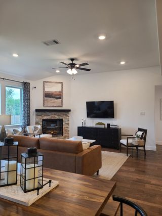 A cozy living room with a stone fireplace, sleek TV setup, and warm brown seating, accented by modern lighting and decor.