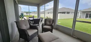 A cozy screened patio with wicker seating, dining area, and a view of the fenced backyard. Perfect for relaxation and entertaining.