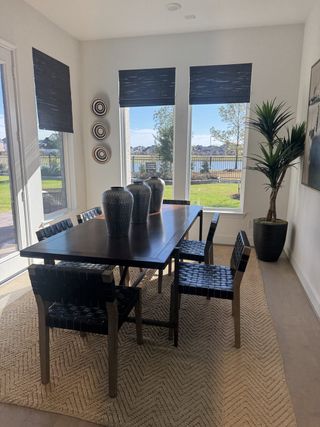 A chic dining room with a sleek dark table, woven chairs, and large windows offering serene water views.