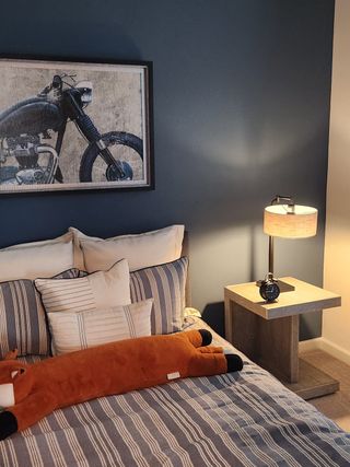 A cozy bedroom with a plush bed, blue accent wall, motorcycle artwork, and a stylish lamp on a wooden nightstand.