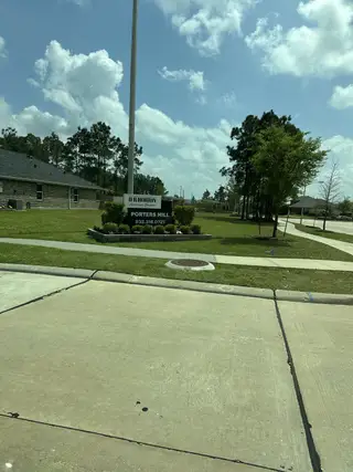 A serene street view in Porters Mill by D.R. Horton, featuring a lush green landscape and inviting signage (New Caney, TX).