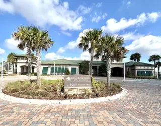 A beautiful entrance to the Indian River Preserve Golf Clubhouse, featuring palm trees, a circular driveway, and elegant architecture that embodies luxury and leisure.