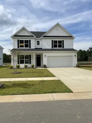 A charming white two-story home with black shutters and lush lawn in Parker's Preserve by Eastwood Homes (Ridgeville, SC).
