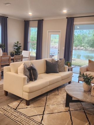 Model Home A cozy living room with a cream sofa, patterned rug, and large windows overlooking a serene pond.