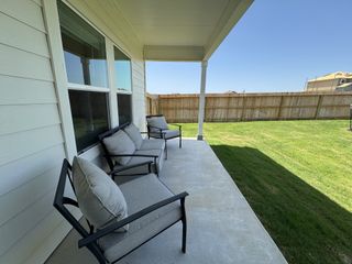 A cozy patio with cushioned seating, overlooking a fenced yard and vibrant lawn.