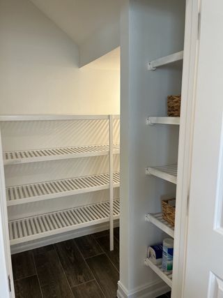 A spacious pantry with sleek white shelving and dark wood flooring, offering ample storage and bright lighting.