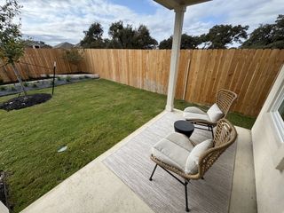 A cozy patio with wicker chairs, a small round table, and a view of a neatly manicured lawn and wooden fence.