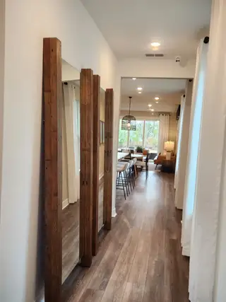 A modern hallway with wood accents, hardwood floors, elegant lighting, and a view into a cozy dining area.