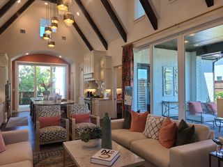 A modern living area with vaulted ceilings, chic lighting, and a cozy seating arrangement overlooking a bright kitchen.