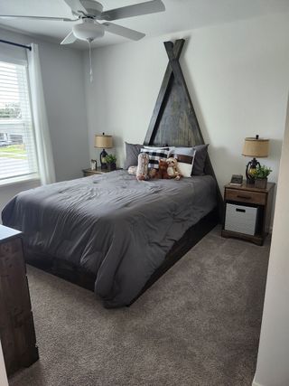 Cozy bedroom with a unique wooden headboard, plush gray bedding, and soft carpet flooring, creating a warm and inviting atmosphere.