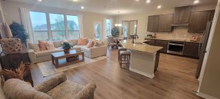 A warm and inviting open-concept living space in a Hidden Bluffs at TRP home, featuring a comfortable sectional sofa, a modern kitchen with a large island, and ample natural light (San Antonio, TX).