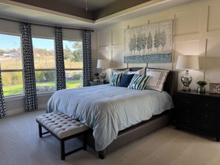 A serene bedroom with large windows, patterned curtains, a cozy bed, and tasteful artwork.