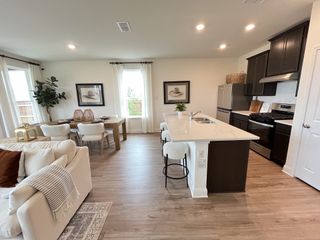 A modern kitchen and dining area with sleek dark cabinets, an island, and cozy seating. Warm tones and natural light abound.