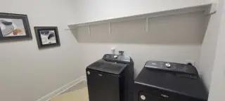 A modern laundry room featuring sleek black appliances, abstract wall art, and a convenient shelf.