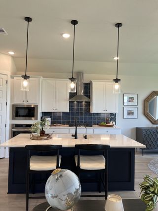 Model Home Modern kitchen with white cabinetry, navy island, pendant lighting, and a sleek backsplash.