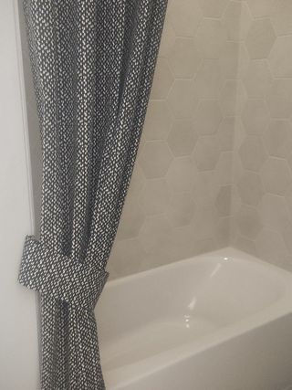 A modern bathroom with hexagonal tile walls and a sleek white bathtub, complemented by a patterned shower curtain.