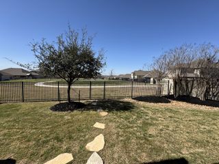 A scenic backyard view with manicured lawns, trees, and a metal fence in Foxbrook by Coventry Homes (Cibolo, TX).