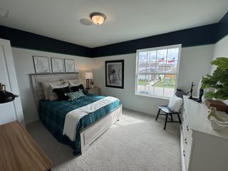 A cozy bedroom with leafy decor, plush bedding in green hues, a light wood bed, and ample natural light from a large window.
