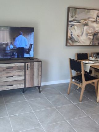 A modern living area with abstract art, a rustic TV stand, and a cozy dining setup on sleek tiled flooring.