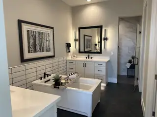 Model Home A spa-like bathroom with a freestanding tub, dual vanities, sleek black fixtures, and a stylish tile backsplash for a modern touch.