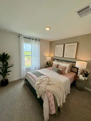 A cozy bedroom featuring a plush bed, stylish decor, soft lighting, and a large window with sheer curtains.