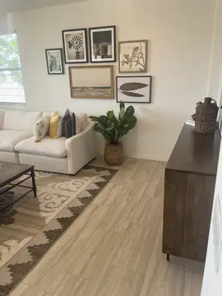 A cozy living room with a white sofa, stylish gallery wall, and patterned rug, accented by a vibrant potted plant.