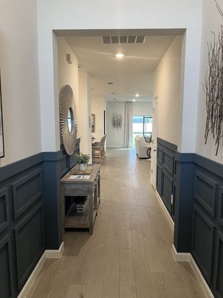 A modern hallway with elegant wood floors, wainscoting, and chic decor leads to a spacious, sunlit living area.