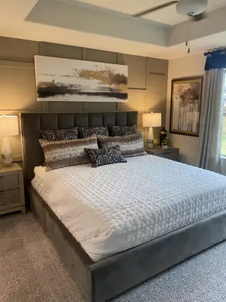 A cozy bedroom with a plush gray bed, abstract wall art, and stylish lamps creating a serene atmosphere.