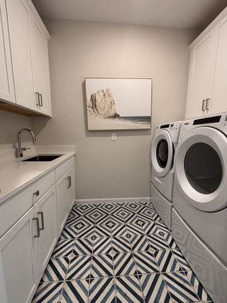 A modern laundry room with patterned tile floor, stacked appliances, sleek cabinetry, and coastal artwork.