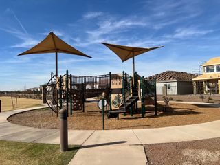 A modern playground with shade structures in El Cidro by Pulte Homes, Goodyear, AZ, set against a clear blue sky.