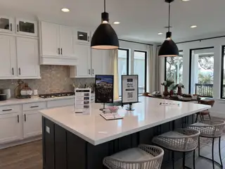 Model Home A modern kitchen with a large quartz island, black pendant lighting, and white cabinetry in Esperanza by Perry Homes (Boerne, TX).