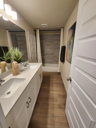 A modern bathroom with dual sinks, wood-style flooring, and a neutral palette, perfect for relaxing and unwinding.