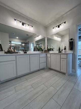 Luxurious bathroom with dual sinks, large mirrors, bright lighting, and a walk-in shower, featuring modern finishes.
