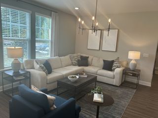 Model Home A cozy living room with a beige sectional, chic black chandelier, and soft lighting from modern table lamps.