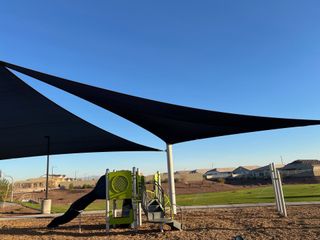 A modern playground with shade sails in Copper Falls by D.R. Horton, Buckeye, AZ, offering a fun outdoor space.