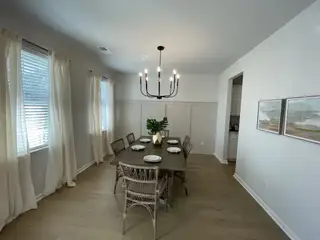 A cozy dining room with a dark wood table, elegant chandelier, and light wood floors, enhanced by natural light and neutral decor.