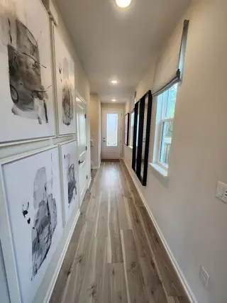 A bright hallway featuring abstract art, light wood flooring, and modern recessed lighting.