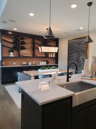 A modern kitchen with sleek black cabinetry, open shelving, stylish pendant lights, and a chic dining nook.