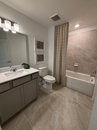 A contemporary bathroom with a white vanity, subway-tiled bathtub, and elegant lighting in Emerald Pointe by Pulte Homes (Apopka, FL).