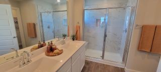 A modern bathroom featuring a sleek double vanity, marble shower, and warm wood flooring.