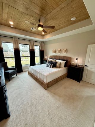 A cozy bedroom with wood-accented ceiling, elegant bedding, and soft carpet, bathed in natural light from large windows.
